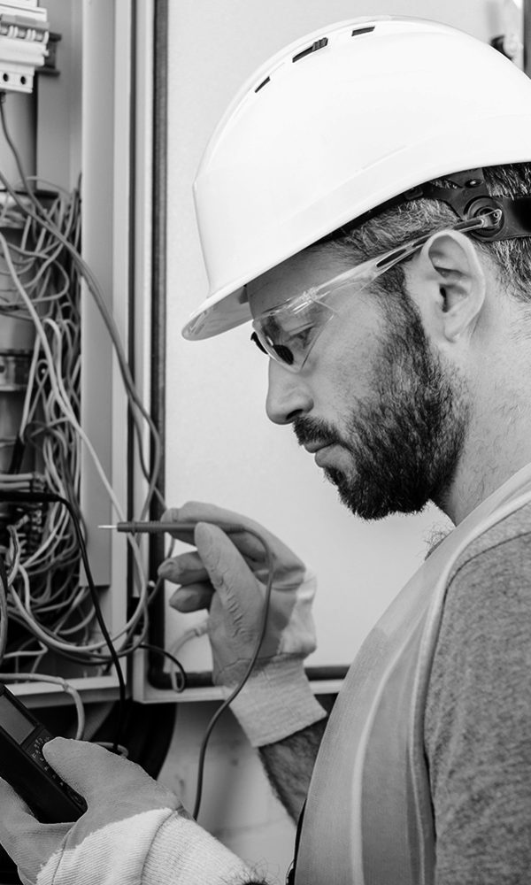 handsome electrician checking electrical box with multimetr in corridor